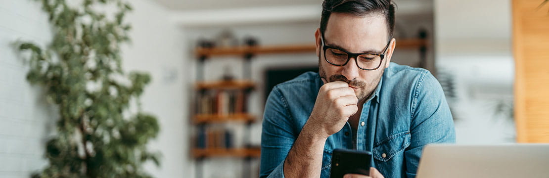 Portrait of a puzzled man looking at smart phone, sitting at table at home. 